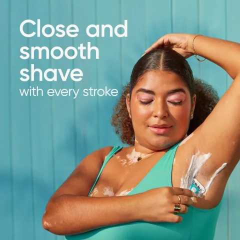 Woman in teal swimsuit shaving her underarm against a blue background.