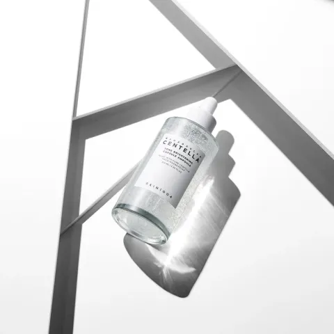 Clear serum bottle casting a shadow on a white geometric surface.