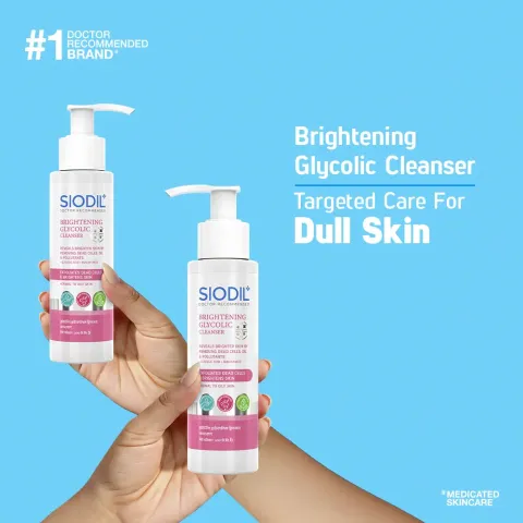 Two hands holding bottles of Siodic brightening glycolic cleanser against a blue background.