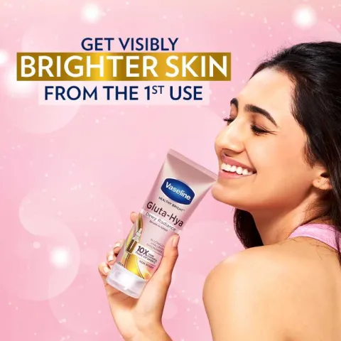 Smiling woman holding Vaseline lotion against a pink background.