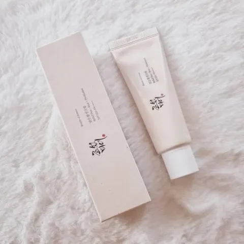 A beige skincare tube and matching box on a soft white textured surface.