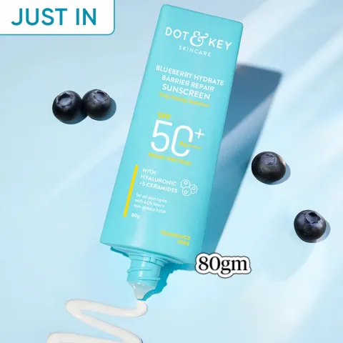 Blue tube of Dot & Key sunscreen with blueberries and sunscreen cream on a light blue background.