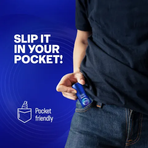 Person placing a small blue spray can into the front pocket of jeans against a blue background.