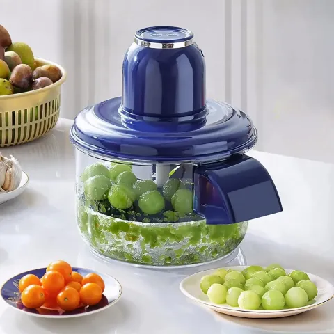 Blue food chopper with green fruit inside, surrounded by plates of assorted fruit.
