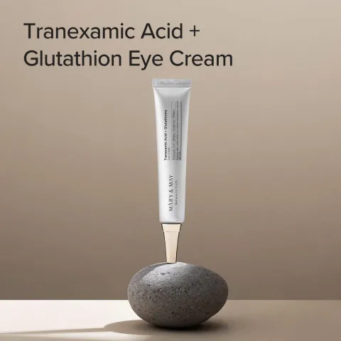 Eye cream tube balanced upright on a smooth gray stone against a beige background.