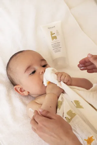 Adult gently wiping a baby’s nose with a soft cloth on a white blanket.