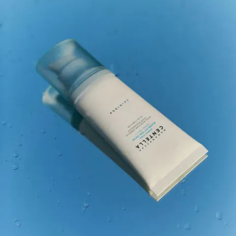 White skincare product bottle with blue cap on a blue background with water droplets.