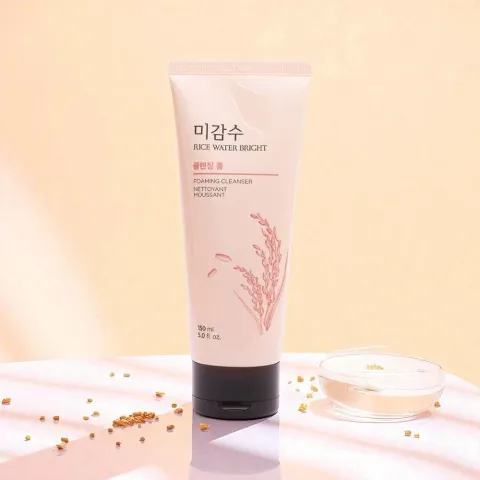 Tube of skincare cream with a black cap, standing on a light peach surface with seeds nearby.