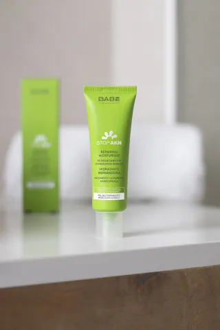 Green skincare tube and box on a white bathroom counter with blurred background.