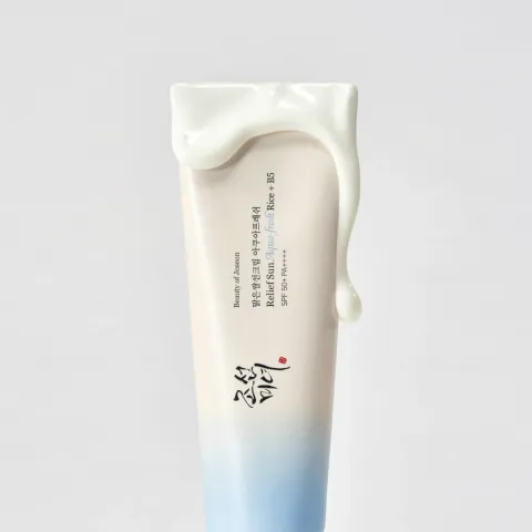 Skincare cream tube with white cream on the top against a light gray background.