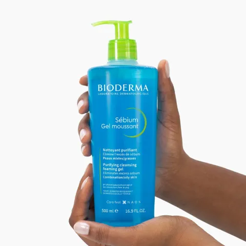 Hands holding a blue Bioderma Sébium gel cleanser bottle with a green pump.