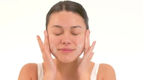 Woman with closed eyes gently touching her face with both hands against a white background.