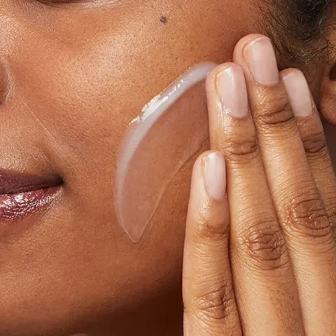 Fingers applying clear gel moisturizer to a woman's cheek.