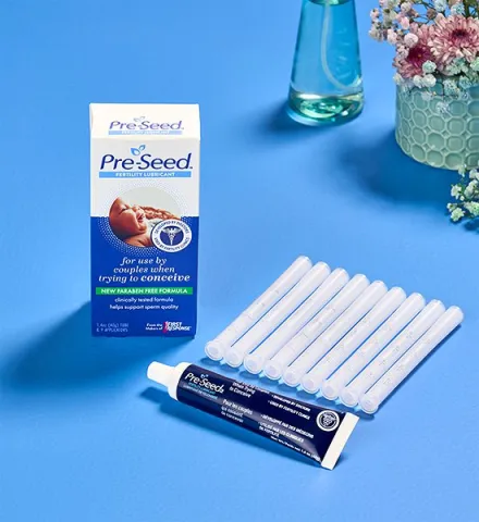 Pre-Seed lubricant box, tube, and applicators on a blue surface with flowers in the background.