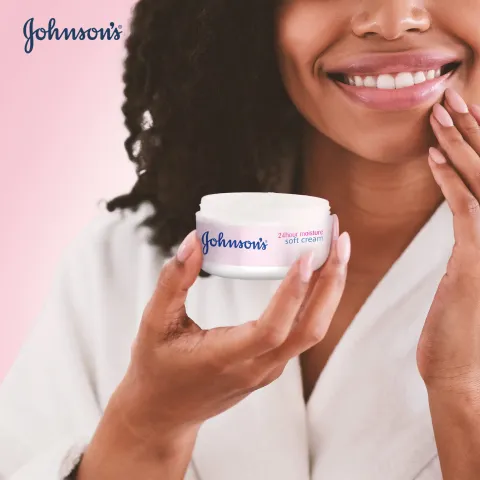 Smiling woman holding Johnson's cream jar against a soft pink background.