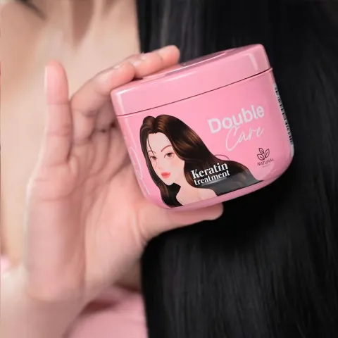 Hand holding a pink hair care product jar near long, smooth black hair.