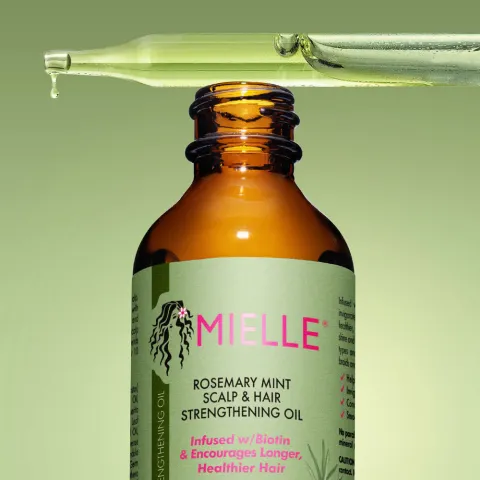 Brown bottle of Mielle rosemary mint hair oil with a dropper above it against a green background.
