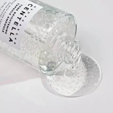 Clear gel-like serum spilling from an open transparent bottle onto a white surface.