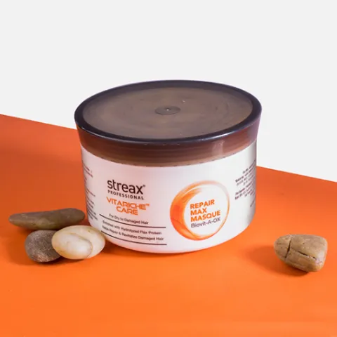 Hair mask container with brown lid on orange surface, surrounded by smooth stones.