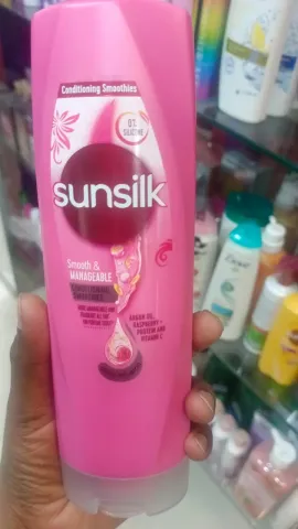 Hand holding a pink Sunsilk shampoo bottle in a store aisle with other hair products.