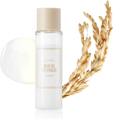 Clear bottle of skincare toner next to rice grains and a liquid droplet.