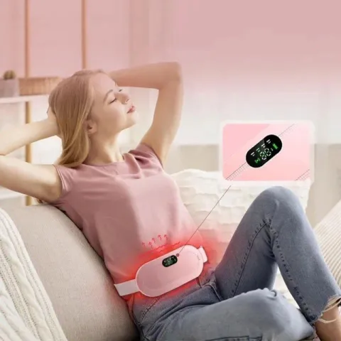 Woman relaxing on a couch using a pink heating pad belt on her abdomen.