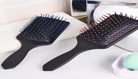 Black paddle hairbrushes with colored bristles on a bathroom counter.