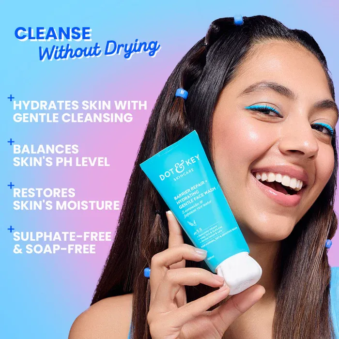 Smiling woman with blue hair clips holding Dot & Key face cleanser against a blue background.