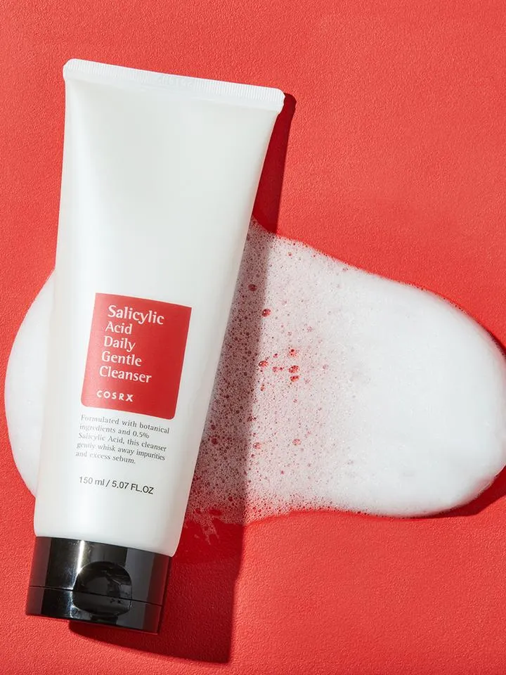 White tube cleanser with black cap on red background, surrounded by foamy lather.