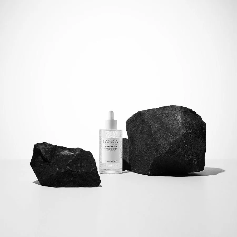 Clear dropper bottle with white label between two black rocks on a white surface.