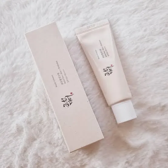 A beige skincare tube and matching box on a soft white textured surface.