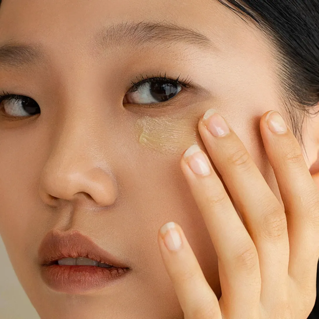 Woman applying concealer under her eye with her fingers.