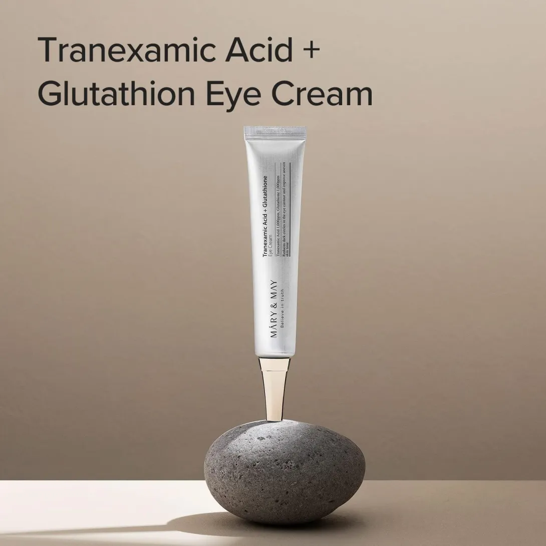 Eye cream tube balanced upright on a smooth gray stone against a beige background.