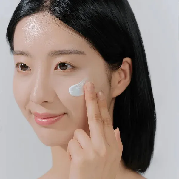 Woman applying cream to her cheek with two fingers, smiling softly.