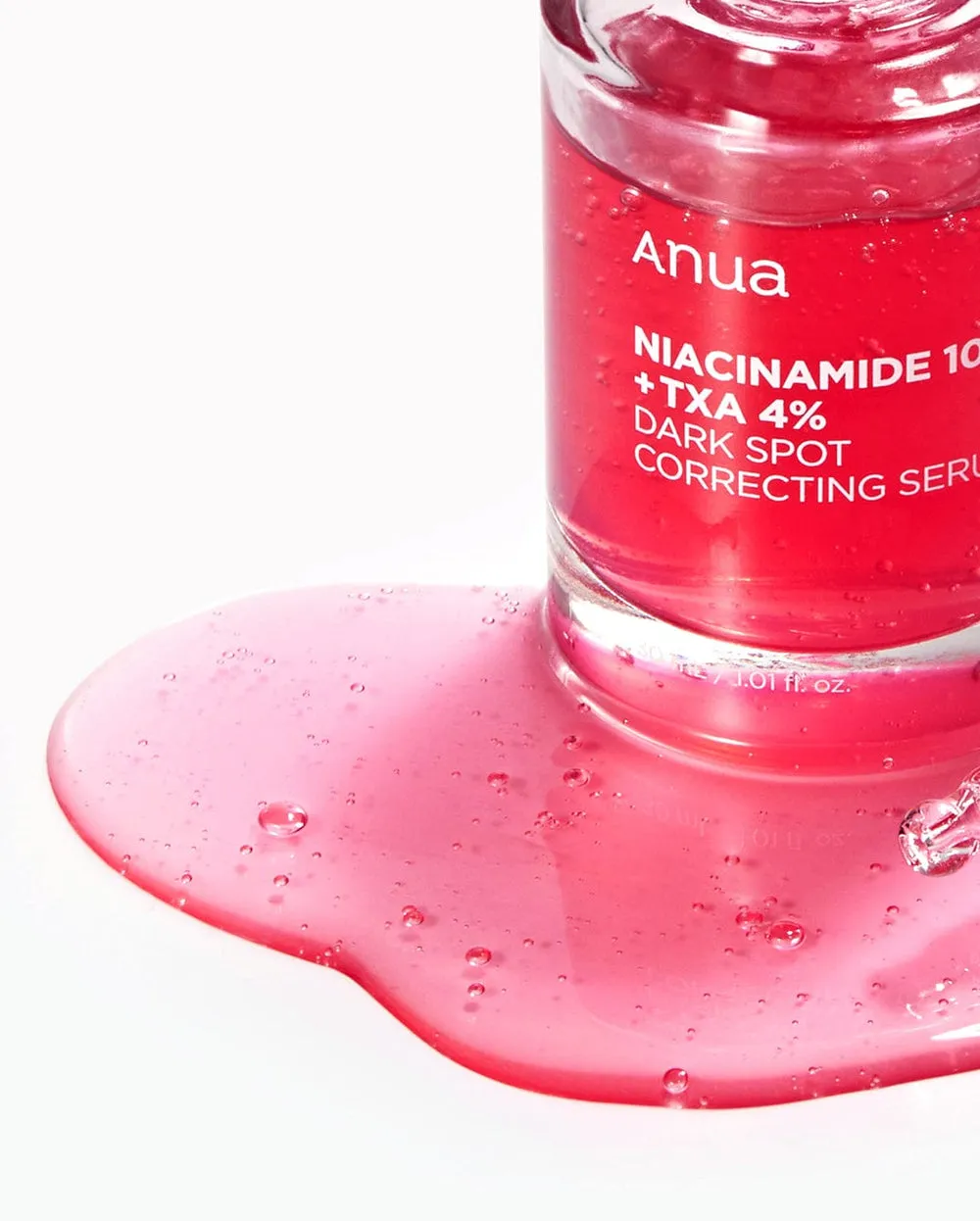 Pink serum bottle tipped over with liquid spilled on a white surface.