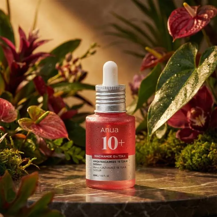 Red serum bottle with dropper on a marble surface, surrounded by green and red plants.