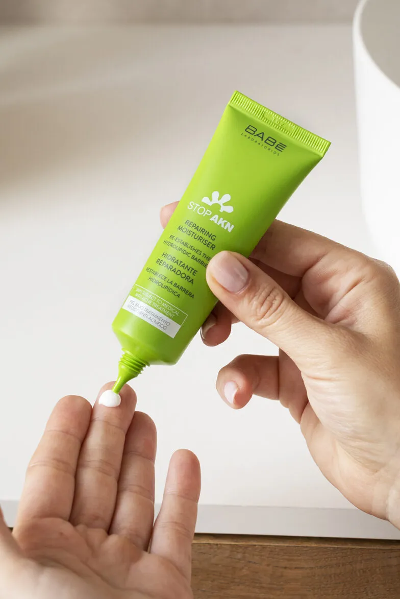 Person squeezing cream from a green tube onto their hand.