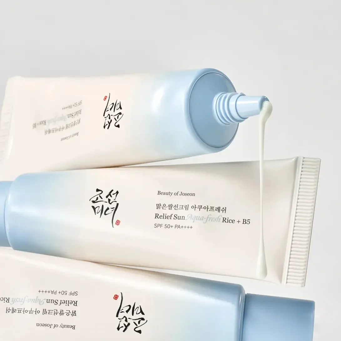 Cream tube with blue cap and Korean text, dispensing white cream, on a light background.