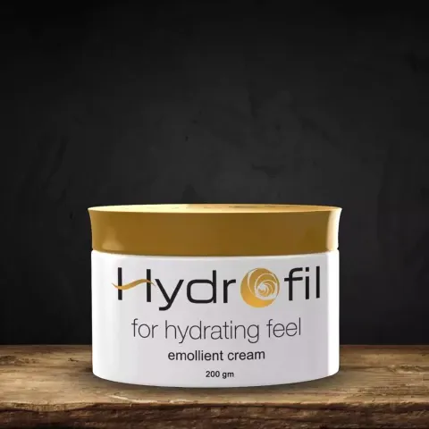Hydrofil emollient cream tub with gold lid on a wooden surface, black background.