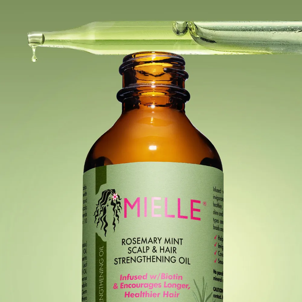 Brown bottle of Mielle rosemary mint hair oil with a dropper above it against a green background.