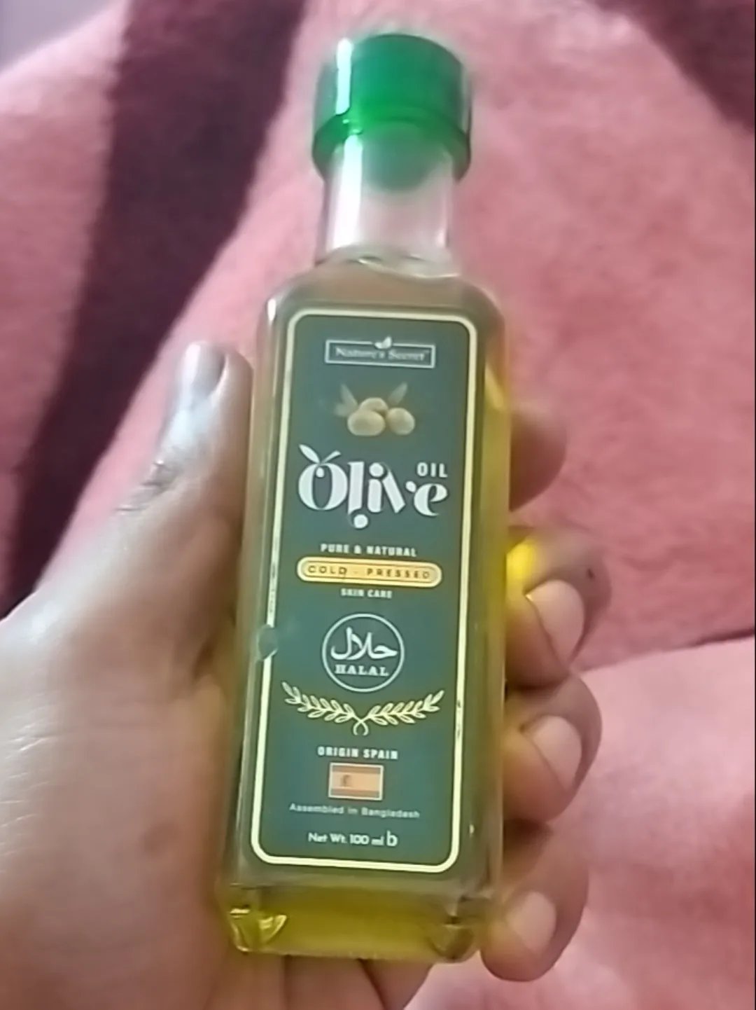 Hand holding a bottle of olive oil with a green label and cap.