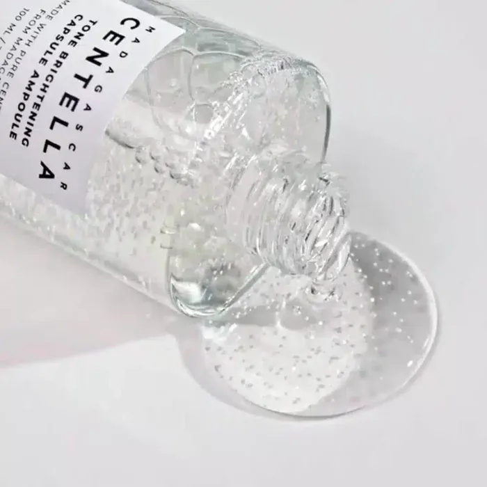 Clear gel-like serum spilling from an open transparent bottle onto a white surface.