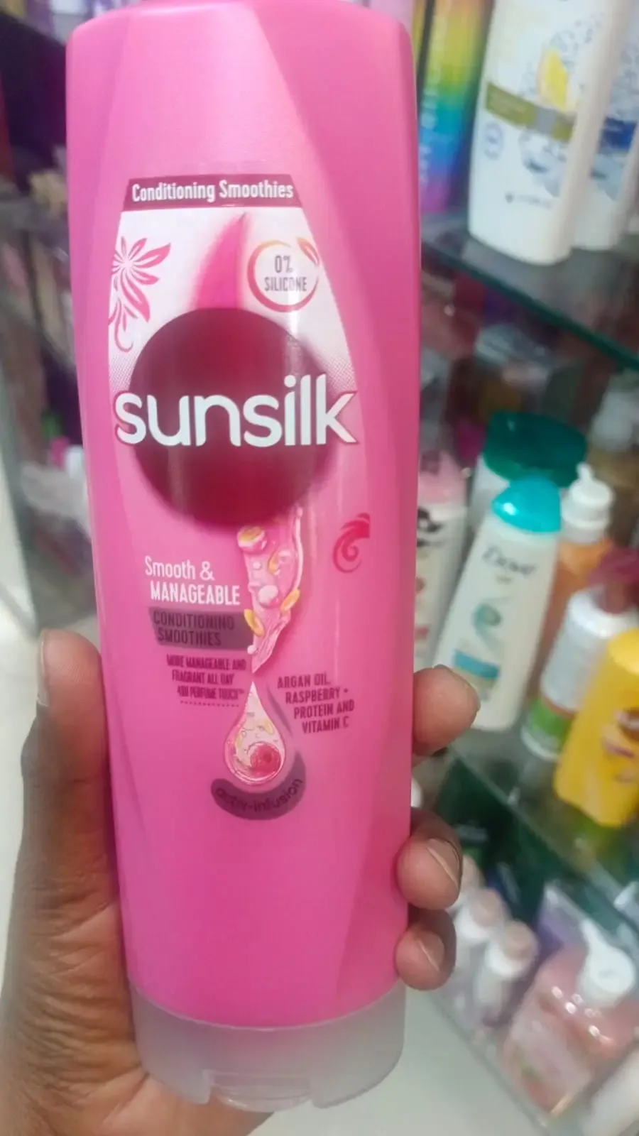 Hand holding a pink Sunsilk shampoo bottle in a store aisle with other hair products.