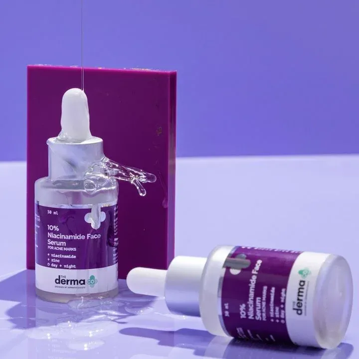Two dropper serum bottles with purple labels and a matching box on a glossy surface.