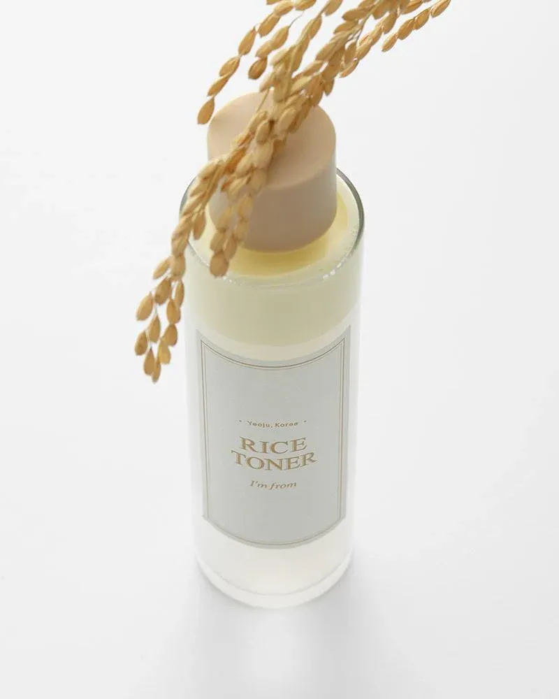 Clear bottle of rice toner with beige cap and rice stalk on top, set against a white background.